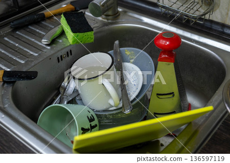 Cluttered kitchen sink with dirty dishes and sponges Cluttered kitchen sink with dirty dishes and sponges 136597119