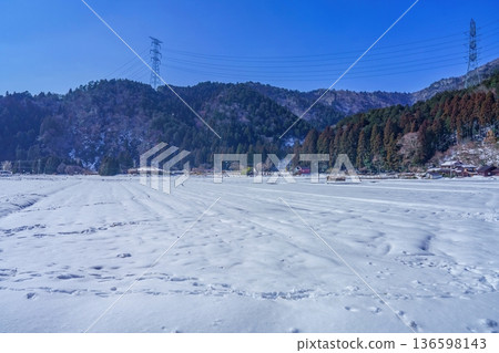 Winter Japanese countryside seen in Miyama Kayabuki Village, snow-covered rice fields and mountains, clear blue sky 136598143