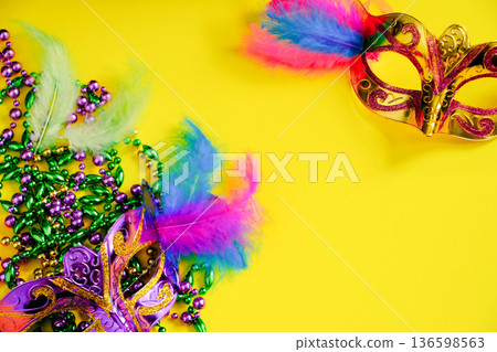 Two carnival masks with feathers on yellow background. Mardi Gras or Fat Tuesday symbol. Multicolored beads Two carnival masks with feathers on yellow background. Mardi Gras or Fat Tuesday symbol. Multicolored beads 136598563
