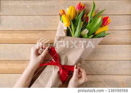 Woman florist ties red bow on large bouquet of colorful tulips. Fresh spring flowers 136598568