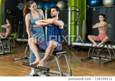 Female trainer guiding young man doing leg presses on pilates chair Female trainer guiding young man doing leg presses on pilates chair 136599212