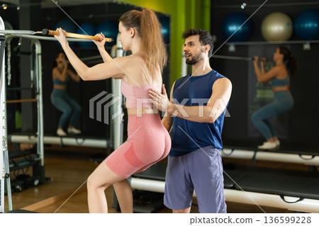 Woman doing a squat on a reformer with the help of a trainer 136599228