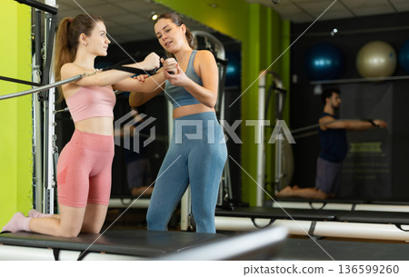 Female trainer guiding girl during arm strength workout on reformer Female trainer guiding girl during arm strength workout on reformer 136599260
