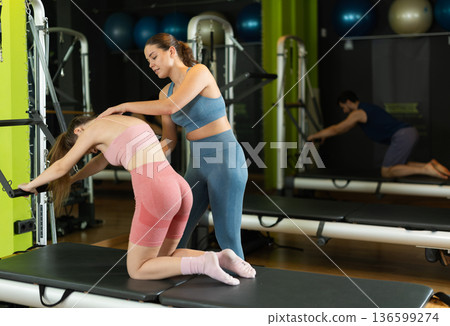 Female trainer guiding girl performing spine stretch on pilates reformer Female trainer guiding girl performing spine stretch on pilates reformer 136599274