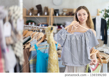 Positive young woman choosing something for summer in clothing store 136599280