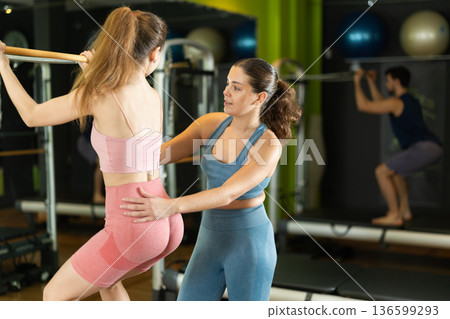 woman doing squats on a reformer with the help of a female trainer 136599293