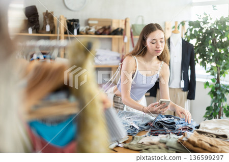 Selective young woman scanning QR-code on pantaloons in clothing store 136599297