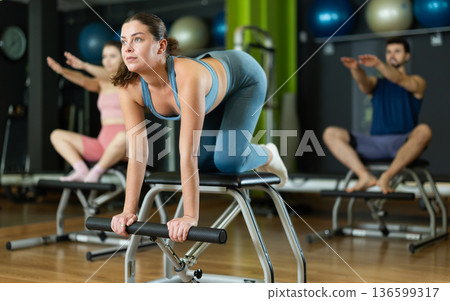 Young woman performing spinal stretch on pilates combo chair 136599317
