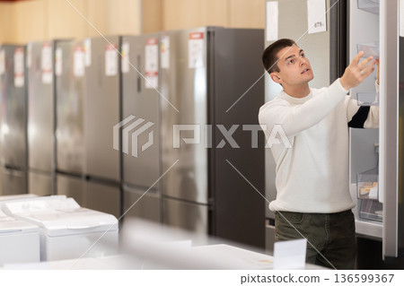 Young man buyer examine fridge in detail before buying Young man buyer examine fridge in detail before buying 136599367