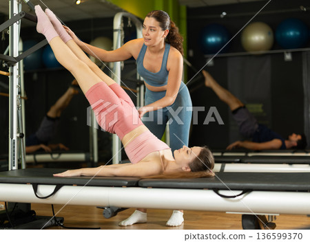 Female trainer guiding girl doing pelvic lift exercise on reformer Female trainer guiding girl doing pelvic lift exercise on reformer 136599370