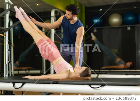 Male trainer helps woman do reformer exercises Male trainer helps woman do reformer exercises 136599372