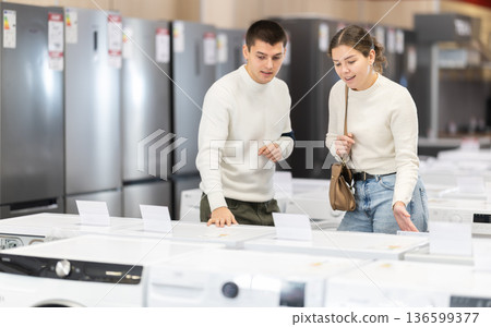 Young couple choosing washing machine or dishwasher Young couple choosing washing machine or dishwasher 136599377