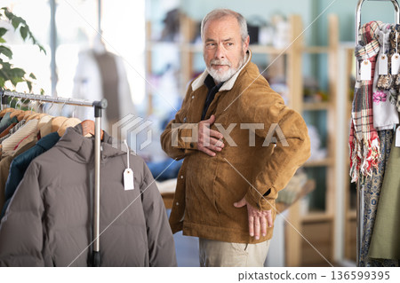 Elderly man trying on brown jacket in store Elderly man trying on brown jacket in store 136599395