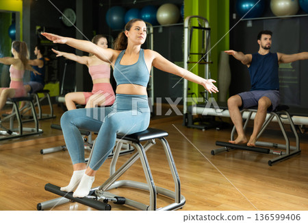 Woman doing arm and leg exercises on chair in Pilates class Woman doing arm and leg exercises on chair in Pilates class 136599406