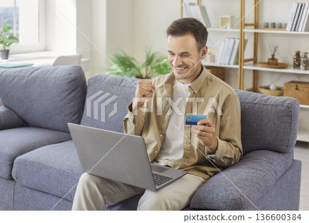 Happy man paying online with credit card at home, celebrating successful purchase Happy man paying online with credit card at home, celebrating successful purchase 136600384