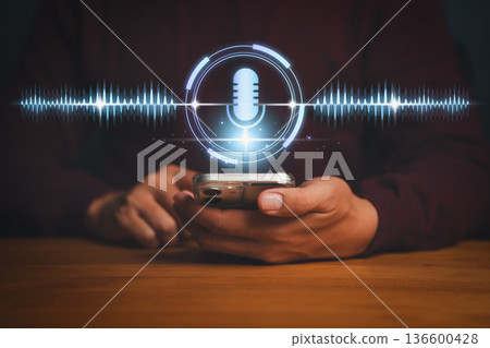 Voice recognition technology concept showing a person using a smartphone with a glowing microphone icon and digital sound waves, symbolizing AI voice assistant, command, and speech analysis. Voice recognition technology concept showing a person using a smartphone with a glowing microphone icon and digital sound waves, symbolizing AI voice assistant, command, and speech analysis. 136600428