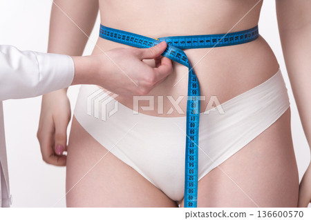 A close-up of a doctor's hand meticulously measuring the dimensions of a patient's waist using a measuring tape. A perfect illustration of the dedication and skill involved in the medical process A close-up of a doctor's hand meticulously measuring the dimensions of a patient's waist using a measuring tape. A perfect illustration of the dedication and skill involved in the medical process 136600570