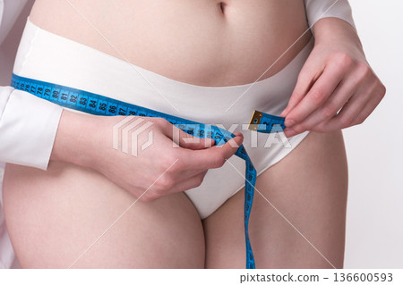 A close-up a female doctor's hands measure the dimensions of a patient's hips using a measuring tape, ensuring accuracy and attention to detail in her examination A close-up a female doctor's hands measure the dimensions of a patient's hips using a measuring tape, ensuring accuracy and attention to detail in her examination 136600593