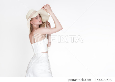 Serene woman with eyes closed in chic white clothing holds straw sun hat. Minimalist studio portrait with bright, high key lighting, neutral colors and ample copy space. Concept of summer fashion Serene woman with eyes closed in chic white clothing holds straw sun hat. Minimalist studio portrait with bright, high key lighting, neutral colors and ample copy space. Concept of summer fashion 136600620