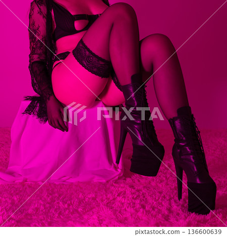 Crop view of sensual woman in black lingerie, stockings and platform boots. Young woman posed confidently in studio with dramatic magenta lighting, creating alluring and modern mood Crop view of sensual woman in black lingerie, stockings and platform boots. Young woman posed confidently in studio with dramatic magenta lighting, creating alluring and modern mood 136600639