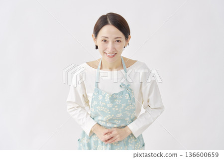 Woman wearing an apron bowing white background looking at camera 136600659