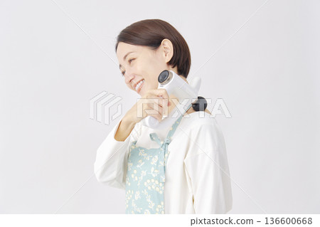 Woman wearing an apron using a massage gun, stiff shoulders, white background Woman wearing an apron using a massage gun, stiff shoulders, white background 136600668