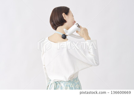 Woman wearing an apron using a massage gun, stiff shoulders, white background Woman wearing an apron using a massage gun, stiff shoulders, white background 136600669