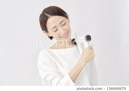 Woman using a massage gun, stiff shoulders, white background Woman using a massage gun, stiff shoulders, white background 136600670