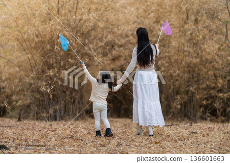 Mother and child girl walking in a dry field with colorful butterfly nets in forest. Mother and child girl walking in a dry field with colorful butterfly nets in forest. 136601663