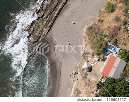 Coastal view of beach, waves, and a house near the shore at noon 136602557