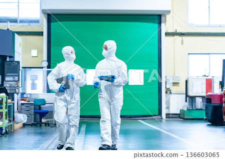 Male and female workers in protective clothing walking through a factory 136603065