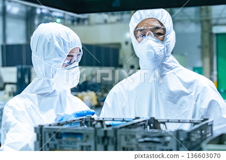Male and female workers wearing protective clothing working in a factory Male and female workers wearing protective clothing working in a factory 136603070