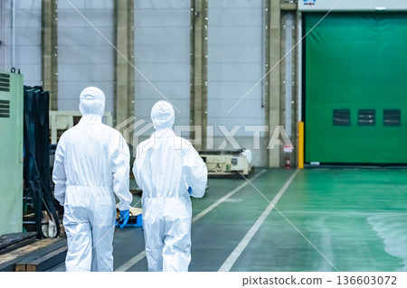 Male and female workers wearing protective clothing walking through a factory Male and female workers wearing protective clothing walking through a factory 136603072