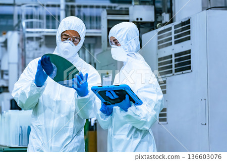 半導體工廠內，身穿防護衣的男女工人手持藥片檢查矽片 136603076