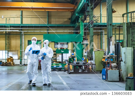Male and female workers in protective clothing walking through a factory Male and female workers in protective clothing walking through a factory 136603083