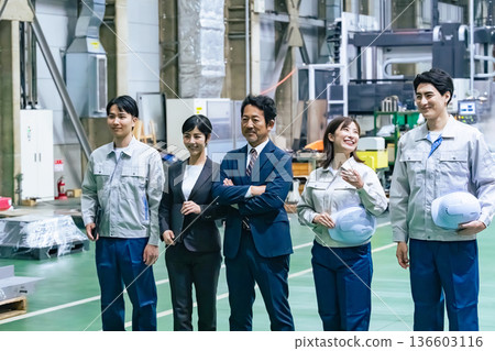 A group of workers standing in a factory A group of workers standing in a factory 136603116