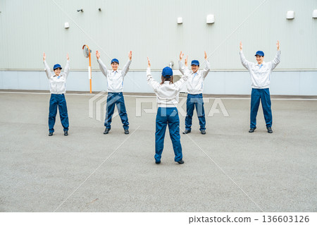 A group of workers doing exercises in front of a factory 136603126