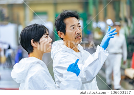 Male and female workers in protective clothing inspecting a factory Male and female workers in protective clothing inspecting a factory 136603137