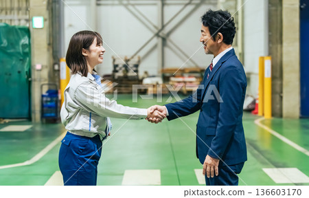A male business person and a female worker shaking hands in a factory A male business person and a female worker shaking hands in a factory 136603170