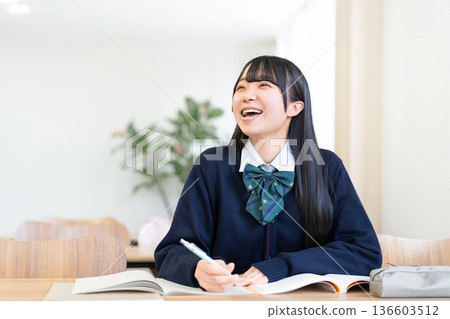 Smiling female high school student studying positively in a bright classroom Smiling female high school student studying positively in a bright classroom 136603512