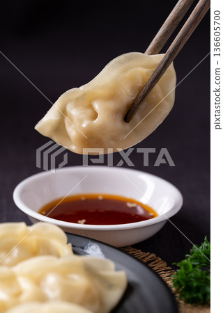 Close up of delicious steamed dumplings being dipped into sesame oil sauce with chopsticks 136605700
