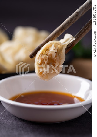 Chopsticks picking up a steamed dumpling with pork and vegetable filling Chopsticks picking up a steamed dumpling with pork and vegetable filling 136605702
