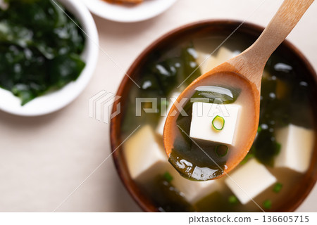 Close up of wooden spoon scooping miso soup with soft tofu and seaweed from a wooden bowl, Top view 136605715