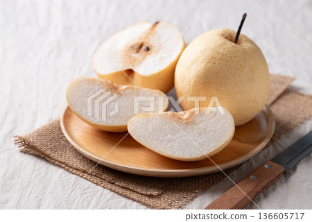 Juicy sliced honey pear on a wooden plate with a kitchen knife on white fabric background 136605717