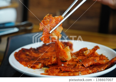 Delicious Crispy Korean Kimchi Pancake (Kimchijeon) Being Picked Up with Silver Chopsticks on a White Plate Delicious Crispy Korean Kimchi Pancake (Kimchijeon) Being Picked Up with Silver Chopsticks on a White Plate 136607007