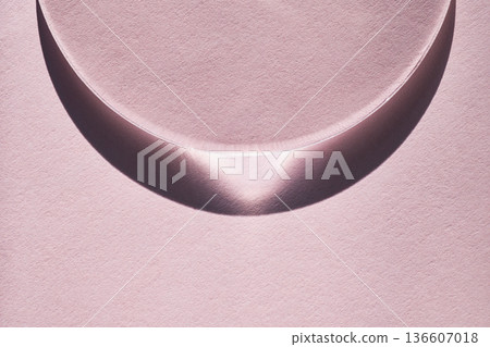 Glass bowl creating crescent shadow with light playing on textured pink paper 136607018