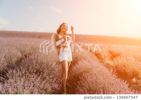 Lavender field woman walking through blooming rows at sunset wearing white summer outfit and straw hat with copy space 136607347