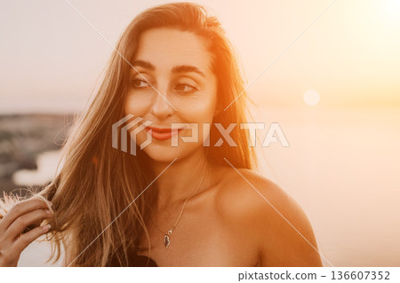 Woman sunset portrait captures a smiling young lady with long hair enjoying the golden light during a peaceful evening by the coast 136607352