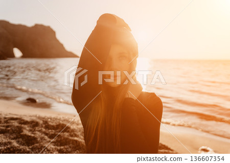 Woman, sunset, beach. Young woman standing on shore during golden hour with strong bright light and moody atmosphere. 136607354