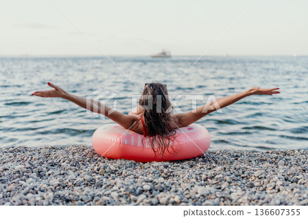 Woman, beach, sea. Relaxing on a pebble beach, a woman enjoys her summer vacation, arms outstretched in freedom. 136607355